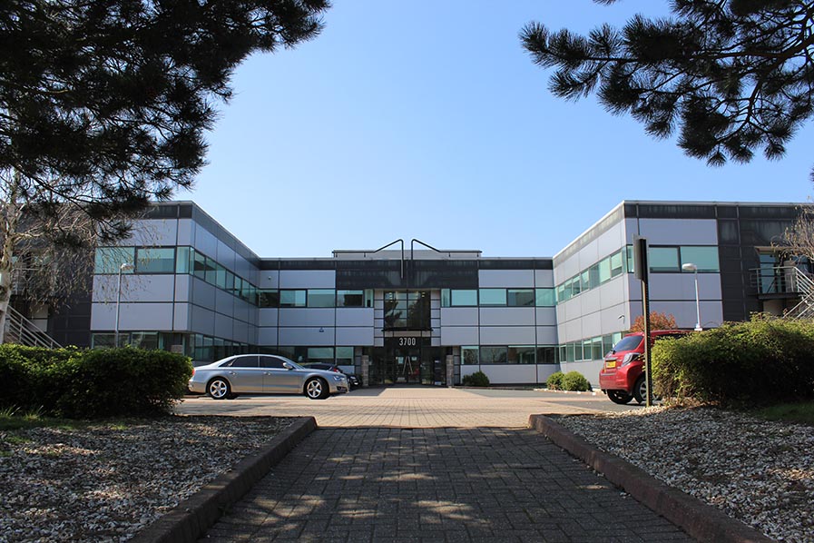 External of 3700 Parkside offices on Birmingham Business Park with trees, bushes and cars in the foreground.