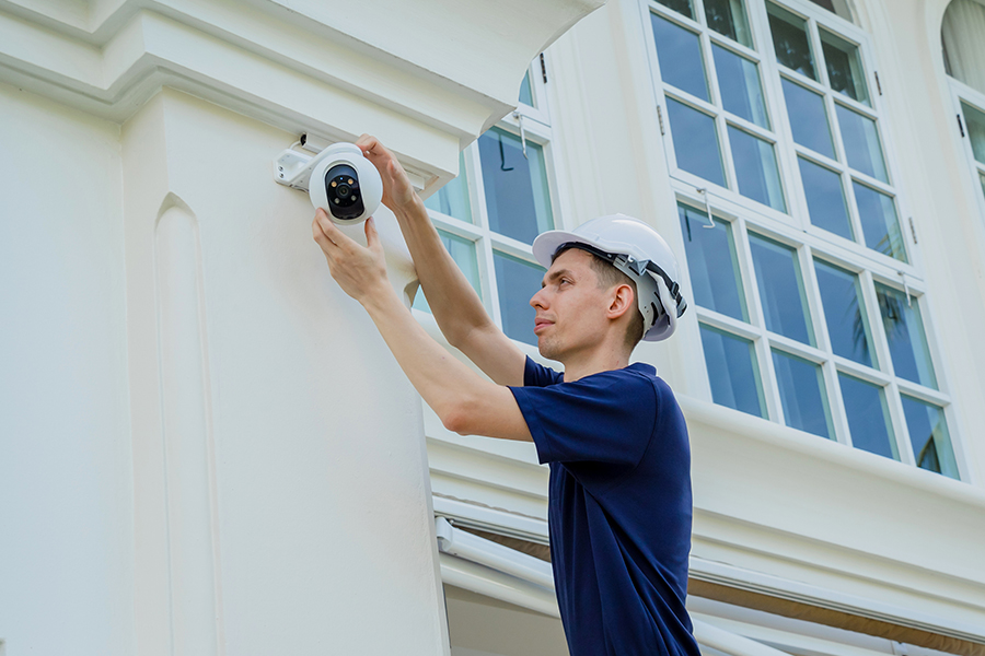 A contractor repairing a security camera on a building to illustrate the range of safety and security management areas that our service covers